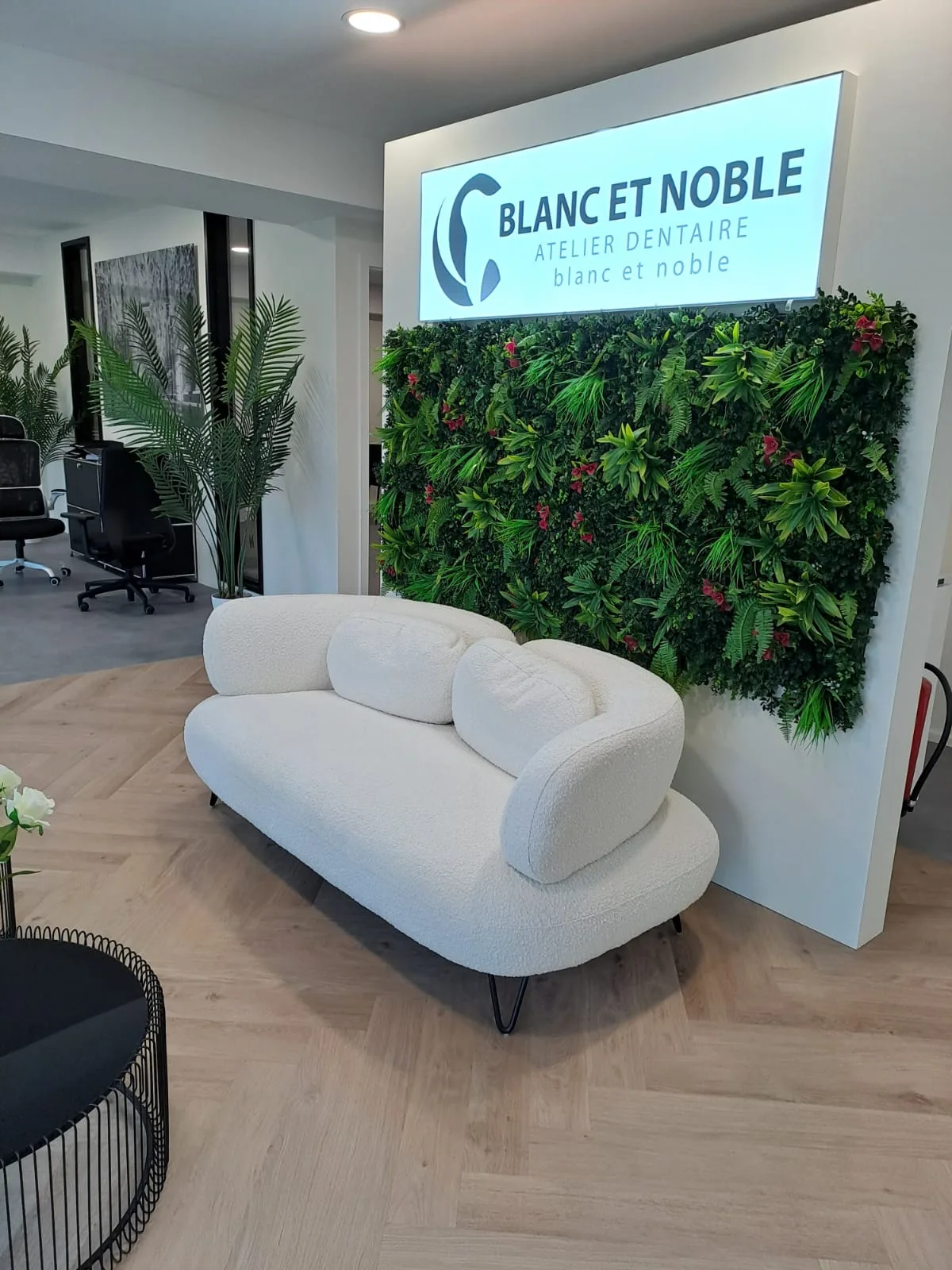 Empfangsbereich von Blanc et Noble mit Sofa, begrünter Wand und beleuchtetem Markenschild
